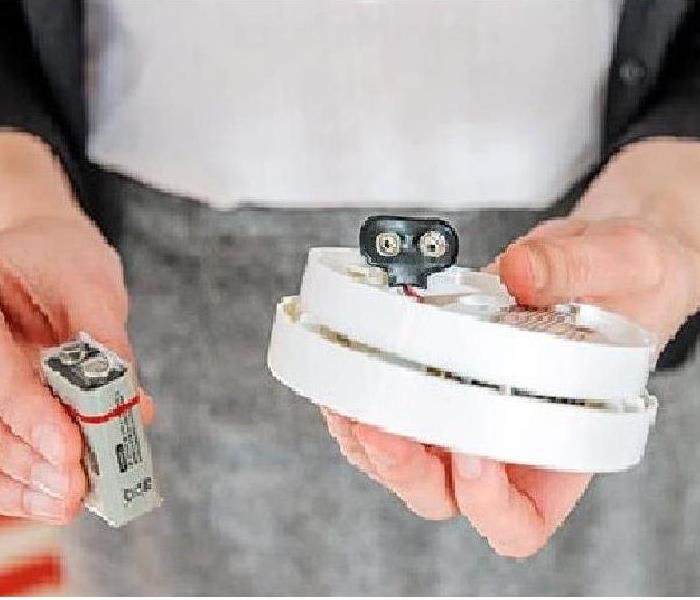 person holding a battery and carbon monoxide detector